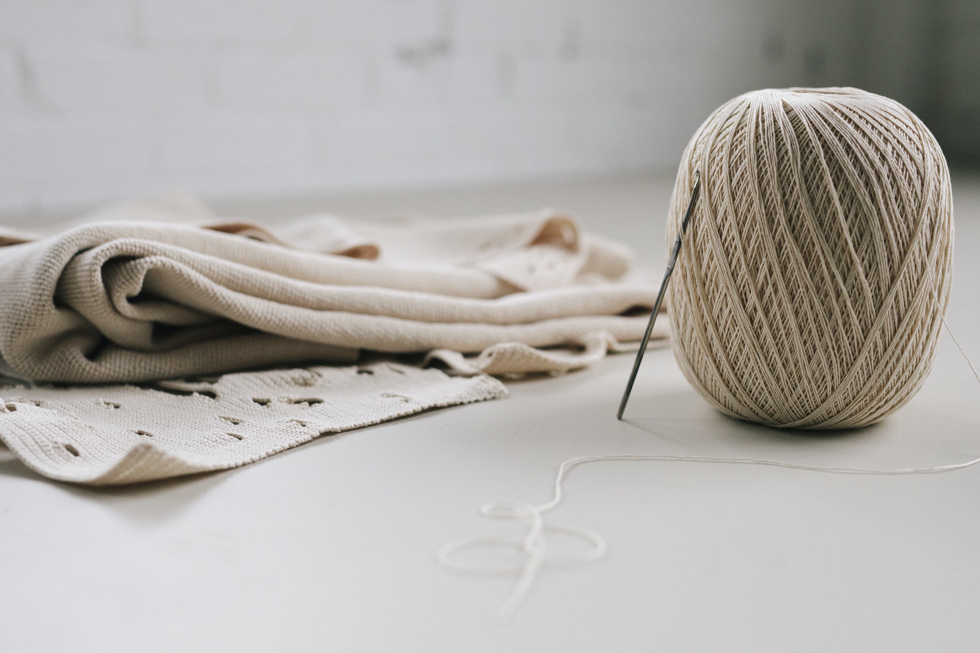 A ball of string or thread and a metal crochet hook or needle with folded fabric.
